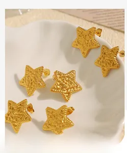 Detail of star-shaped gold earrings with crinkled texture on a white shell plate