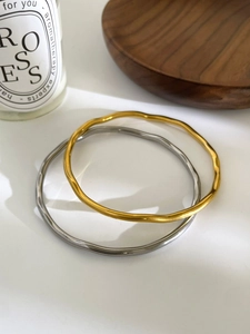 Detail view of wavy 18K gold and silver plated titanium steel bracelets on a wooden tray