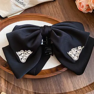 Elegant black satin bow hair claw clip with triangle rhinestones on a wooden tray