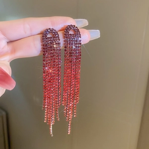 Elegant long tassel earrings with red crystal gradient held against a warm blurry backdrop