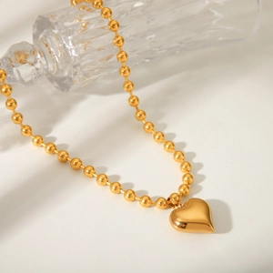 Detailed view of a gold-plated heart pendant on a bead chain over a glass display