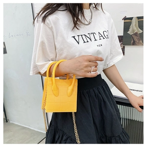Detail of yellow crocodile pattern mini bag with golden chain strap on a model
