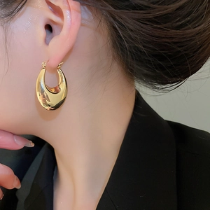 Close-up of polished gold-plated oval hoop earrings worn for a minimalist fashion style