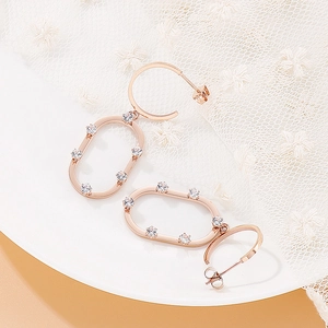 Détail de créoles en or rose avec zircons blancs sur fond de dentelle blanche