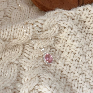 Macro shot of silver necklace with oval pink zircon pendant on a beige knit sweater