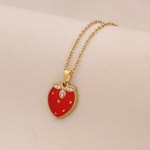Dettaglio di una collana dorata con ciondolo a fragola rossa e foglie in cristallo
