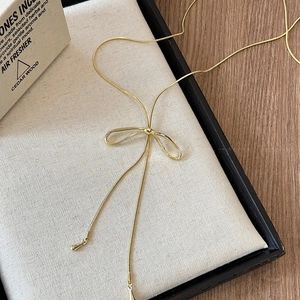 Detail of a gold bow tie necklace with snake chain tassels on a soft fabric display