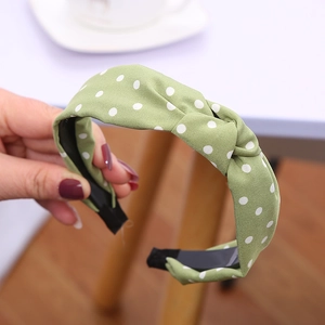 Dettaglio ravvicinato di un cerchietto verde annodato con pois bianchi in tessuto