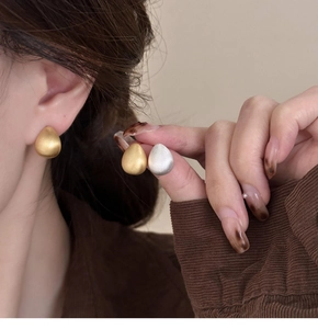Detailed view of matte gold and silver teardrop earrings with brushed metal finish