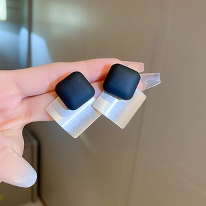Dettaglio macro di orecchini geometrici con elementi quadrati neri opachi e argento spazzolato