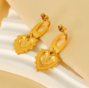 Détail de boucles d'oreilles cœur dorées avec bords radiants et fini mat sur socle
