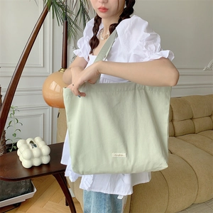 Close-up of a mint green large canvas tote bag held by a model in a cozy home setting