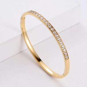 Minimalist gold-plated bangle featuring CNC-set crystals on a sleek white geometric stand