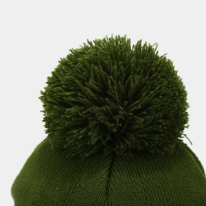 Close-up of the dark green knit beanie featuring a fluffy pom-pom and ribbed texture