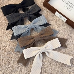 Set of five knitted bow hair clips in elegant neutral tones on a soft plush background