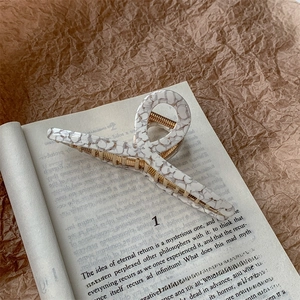 Close-up of marble pattern acetate hair claw clip with gold metal spring on book