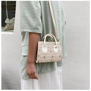 Detail of straw woven handbag with green floral embroidery and beige faux leather strap