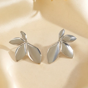 Silver leaf shaped stainless steel stud earrings displayed on beige satin fabric