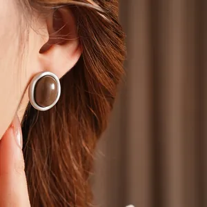 Retro oval silver earrings with brown resin inlay worn by a model on a soft background