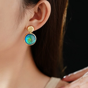Close-up of stylish round blue-green resin earrings with gold accents on model
