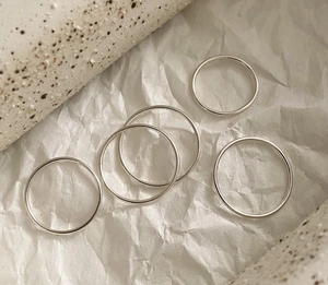 Artistic detail of minimalist polished silver stackable rings on textured paper background