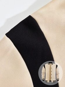 Detailed view of beige and black contrast stitching and knit fabric on a baseball jacket