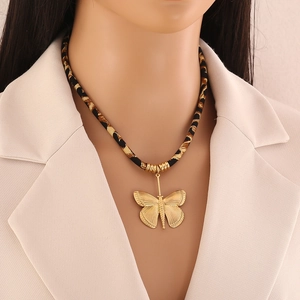 Macro shot of a golden butterfly pendant with black and gold braided rope chain necklace