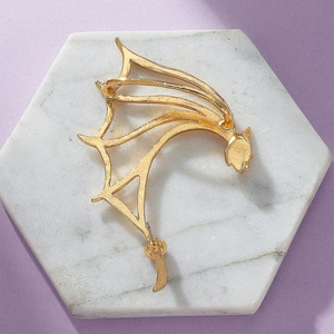 Detail of a golden dragon wing ear cuff on a marble tray with minimalist aesthetic