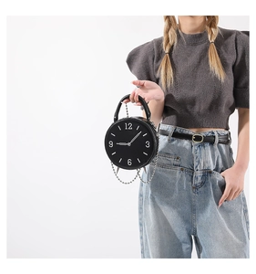 Detail of creative black clock-shaped handbag with metal chain and white numeric markings