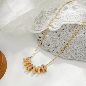 Close-up of golden necklace with sparkling rhinestone MAMA pendant on white surface