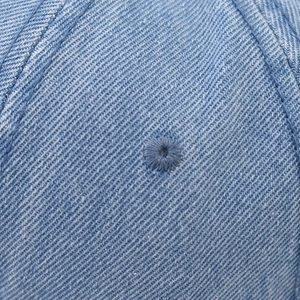 Gros plan du denim bleu délavé avec détail d'un œillet de ventilation brodé sur la casquette
