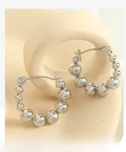 Detailed view of silver beaded hoop earrings on a minimalist beige ceramic display