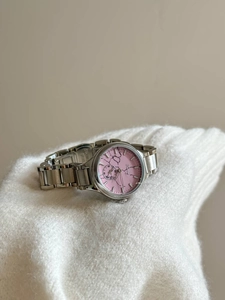 Detail of silver steel lady watch with pink marble dial resting on a white knit sweater