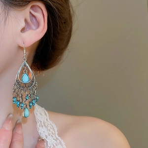 Detail of vintage bohemian drop earrings with turquoise stones and silver tassels on a model