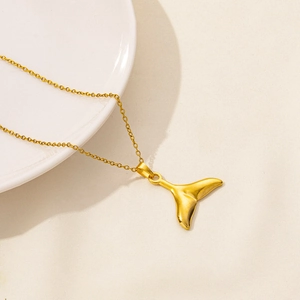 Macro view of golden whale tail pendant on thin steel chain resting on white ceramic