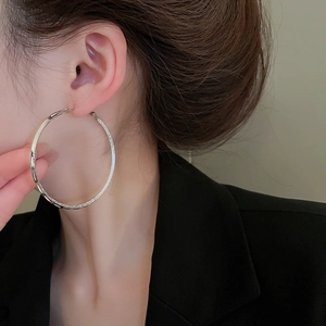 Close-up of large textured silver hoop earrings worn with professional black attire