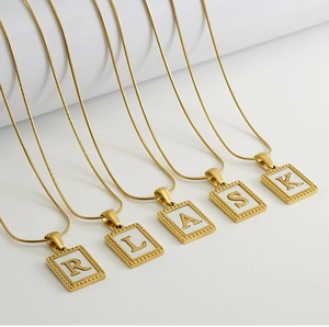 Detailed view of five gold snake chain necklaces with letter-engraved square pendants
