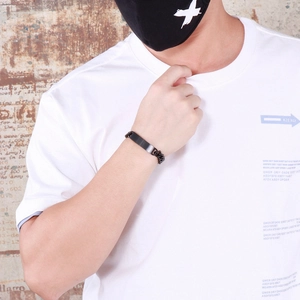 Detail of a black matte stainless steel ID bracelet worn by a model against a stone wall
