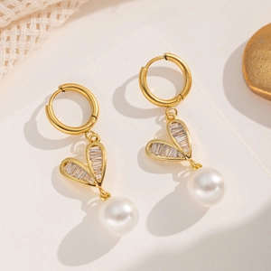 Elegant gold heart earrings with sparkling cubic zirconia and hanging pearls on off-white base