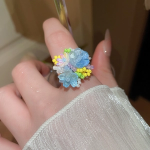 Dettaglio dell'anello a fiori fatto a mano con perline azzurre e bianche sul dito