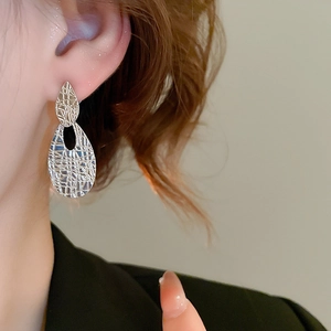 Close-up of silver drop earrings with woven texture worn by model in lifestyle setting