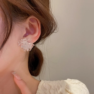 Minimalist resin flower stud earrings with transparent petals on a model’s ear