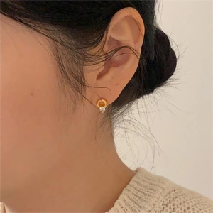 Detail of round gold ear stud with a clear zircon on a model wearing beige knitwear