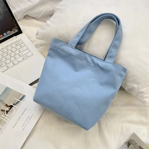 Blue canvas tote bag on bed next to laptop and magazine, showing fabric texture