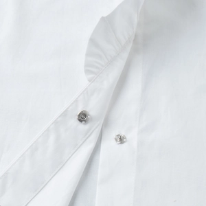 Close-up of white ruffled shirt featuring metal snap buttons and precise stitching details