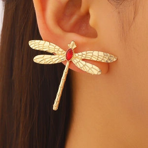 Détail macro d'une boucle d'oreille libellule dorée avec pierre rouge et ailes réalistes