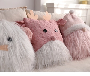 Three assorted plush Christmas pillows featuring deer and gnome designs on a cozy sofa