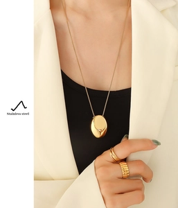Close-up of gold stainless steel oval pendant necklace and rings on a model in a suit