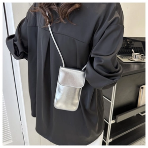 Silver glossy crossbody phone bag worn over a black outfit for a stylish modern look