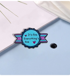Detail view of enamel brooch featuring 'It's fine' text on white book background